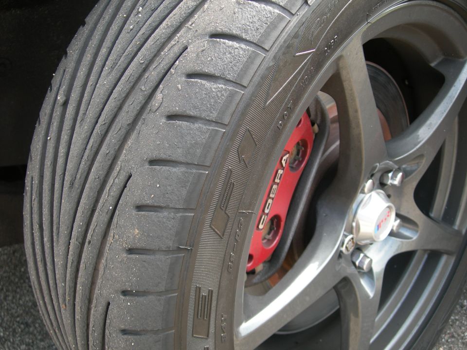 Worn tire and red Cobra brake caliper on a dark gray wheel