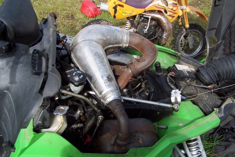 1989 Ford Bronco II - Close-up of a snowmobile's engine and exhaust system, with a dirt bike visible behind it.