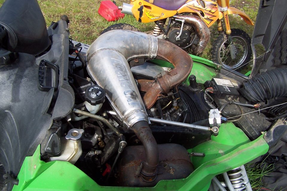 Snowmobile engine bay with large exhaust pipe. Yellow dirt bike in background