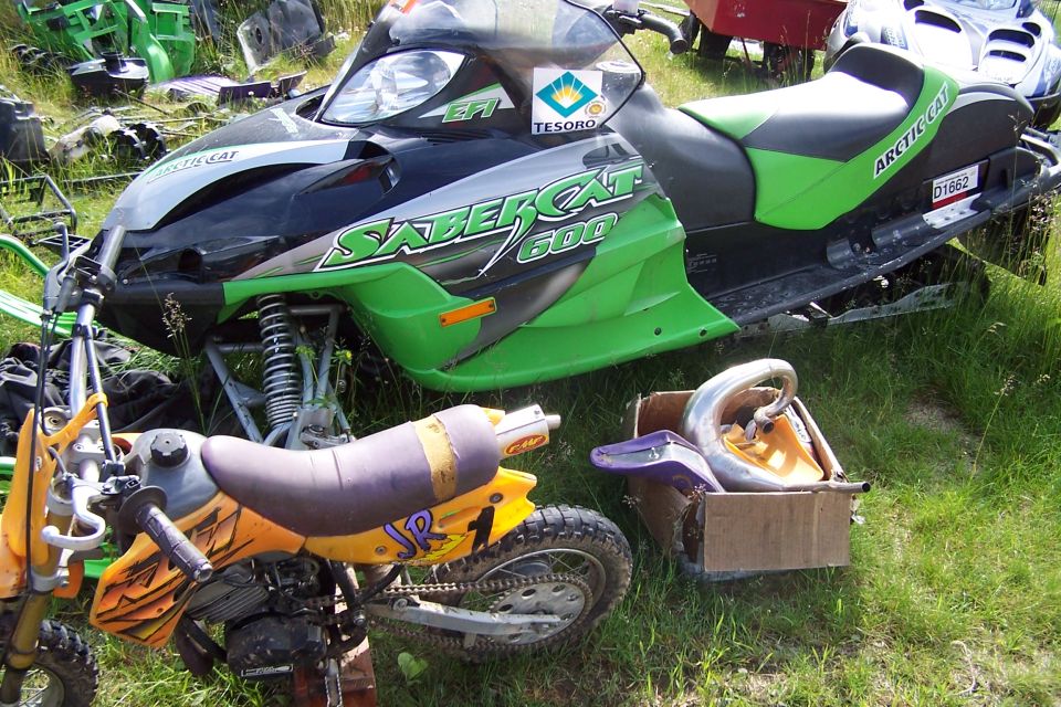 Green and black Arctic Cat Sabercat 600 snowmobile front view with a dirt bike nearby