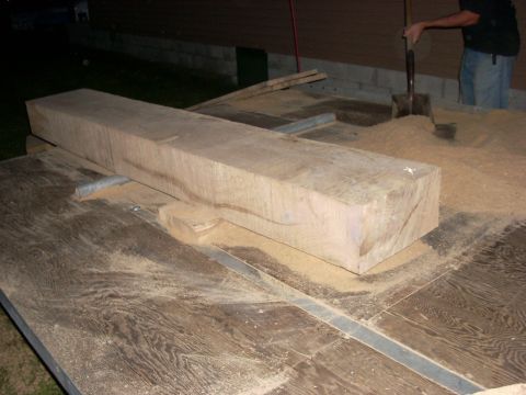 2000 Chevrolet Tahoe - A large wooden beam is positioned on a table saw, surrounded by sawdust, with a person in the background using a shovel.