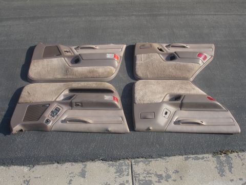 1993 Ford Taurus - Four tan interior door panels from a 1993 Ford Taurus are displayed on a dark asphalt surface.