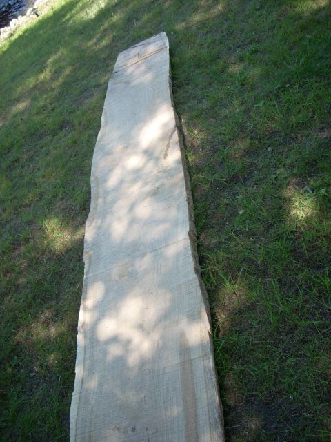 2000 Chevrolet Tahoe - A large, unfinished slab of wood lies on a grassy area, with dappled sunlight creating shadows on its surface.