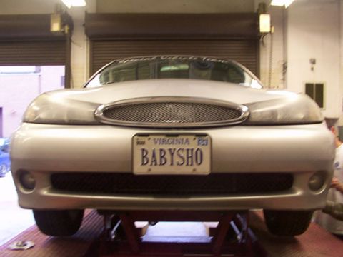 1998 Ford Taurus - The front of a silver sedan is shown, lifted on a rack, with a custom grille and a personalized license plate.