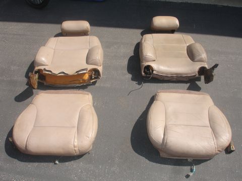 1993 Ford Taurus - Two pairs of tan leather car seats are shown on a paved surface, with one seat showing significant damage to its base.