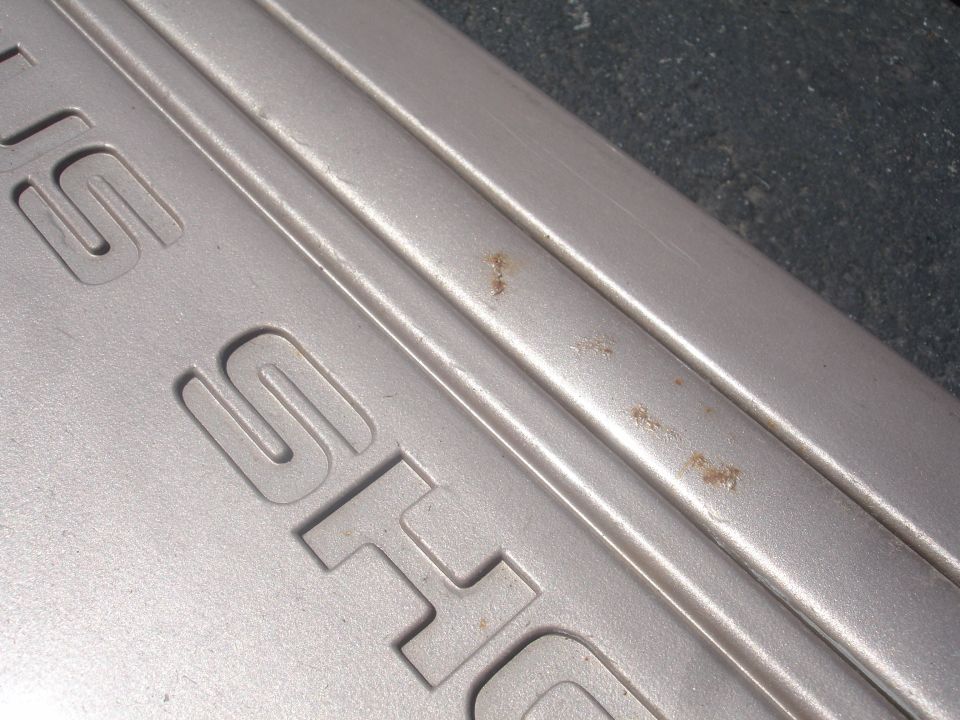 Silver SHO emblem with rust spots on textured surface