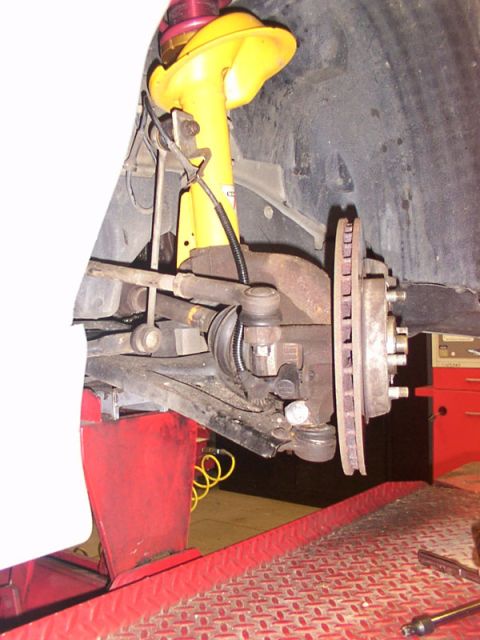 1998 Ford Taurus - The front suspension and brake assembly of a vehicle is shown, with a bright yellow shock absorber visible.