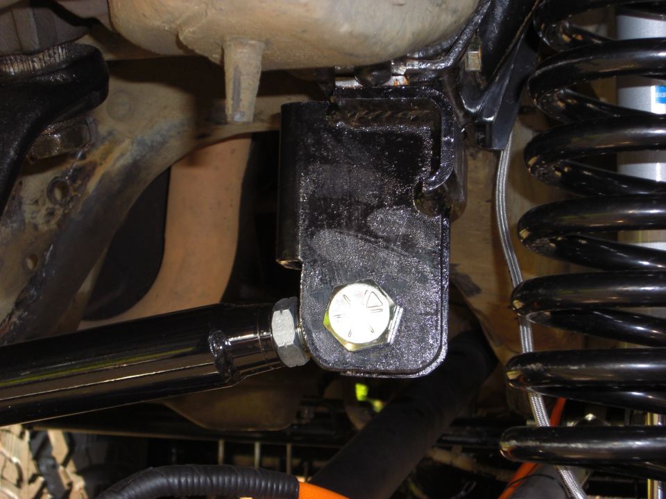Black metal bracket with a silver bolt attached to a shiny black metal rod, near a black coil spring
