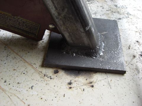 1993 Ford Bronco - Close-up of a welded metal bracket on a flat surface, with some text visible on a maroon component.
