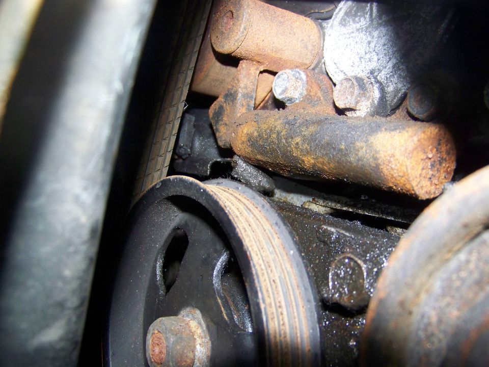 Close-up of a rusty engine component with a pulley and belt, showing oil residue