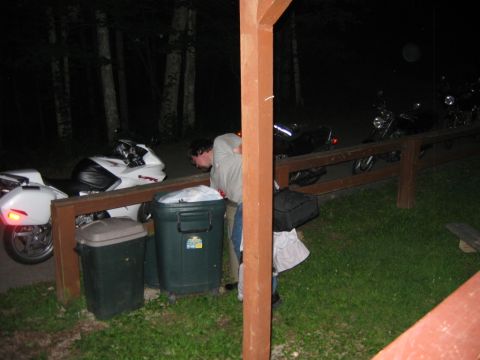 1985 Ford LTD Crown Victoria - Multiple motorcycles are parked in a row at night, with a person tending to trash cans nearby.