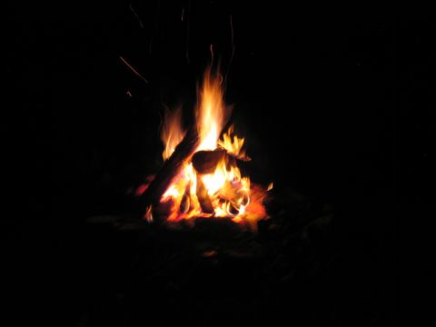 1985 Ford LTD Crown Victoria - A campfire burns brightly in the darkness, with embers and sparks rising into the night sky.