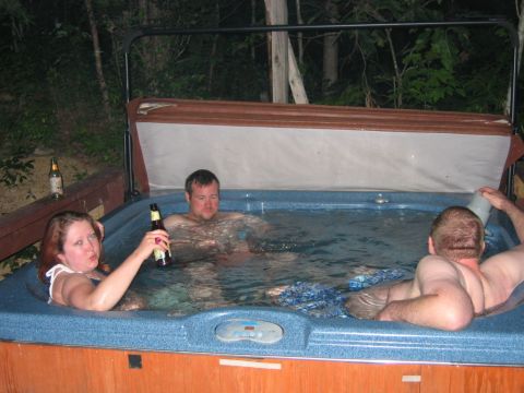 1985 Ford LTD Crown Victoria - Friends enjoy a soak in a hot tub, with drinks in hand, surrounded by trees.