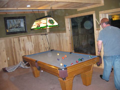 1985 Ford LTD Crown Victoria - A man plays pool in a room with wood paneling and a decorative lamp above the table.