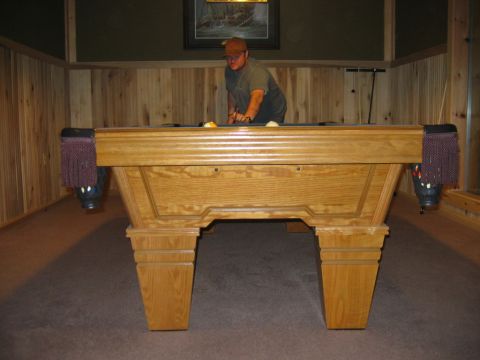 1985 Ford LTD Crown Victoria - A man plays pool at a wooden table in a room with wood-paneled walls.