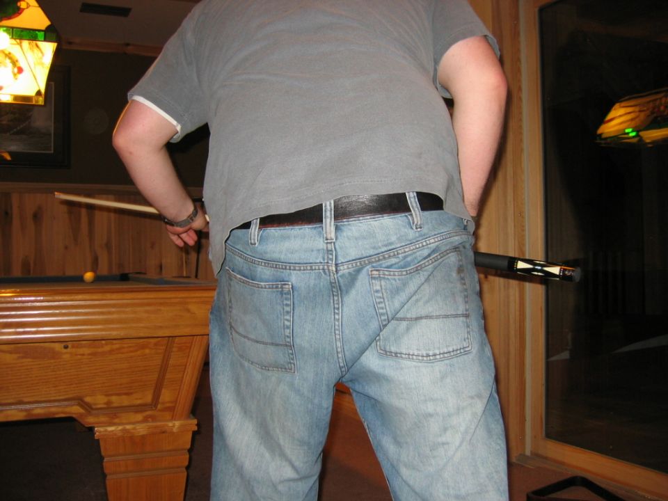 Person in jeans and t-shirt by a pool table, holding a pool cue