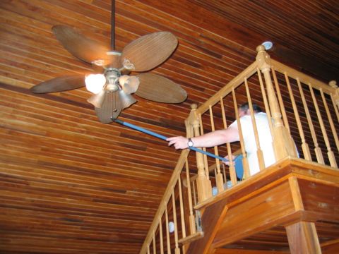 1985 Ford LTD Crown Victoria - A person uses a long pole to clean a ceiling fan in a room with wood-paneled walls and ceiling.