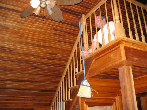 1985 Ford LTD Crown Victoria - A man stands on an upper landing, holding a broom over a wooden staircase with a ceiling fan visible above.