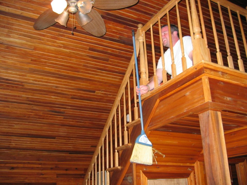 Man on upper level holding a broom over a wooden staircase