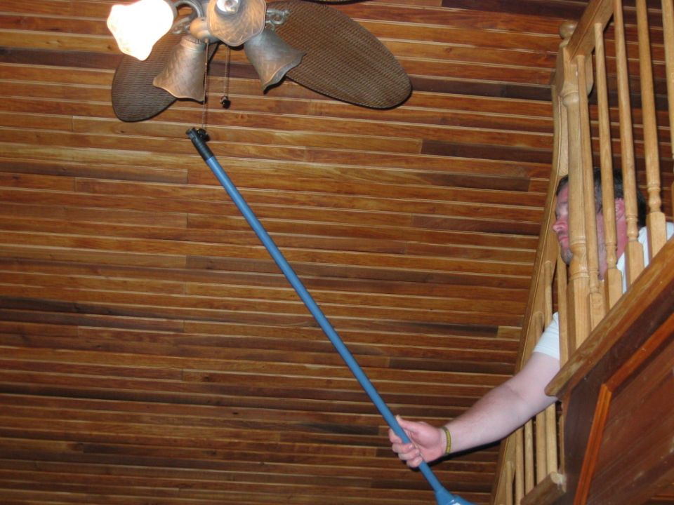 person cleaning ceiling fan with a long pole