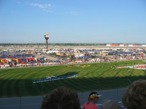 1985 Ford LTD Crown Victoria - A wide view of Chicagoland Speedway during a NASCAR event, showing the track, grandstands, and a large parking area filled with vehicles.