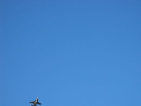 1985 Ford LTD Crown Victoria - A jet airplane is seen in flight against a vast expanse of blue sky.