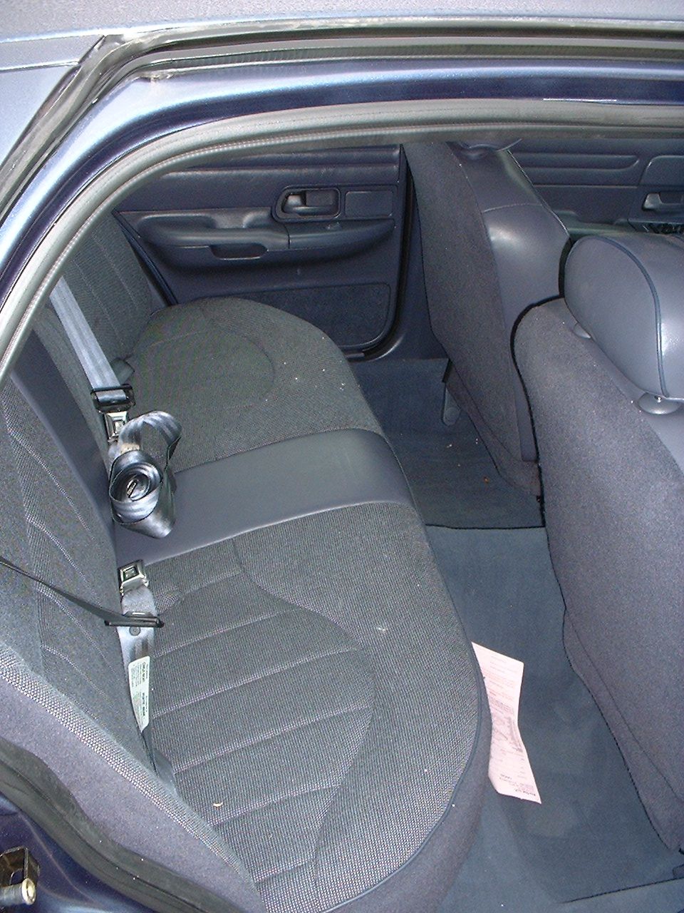 Gray cloth rear bench seat of a sedan with a paper document lying on the floor