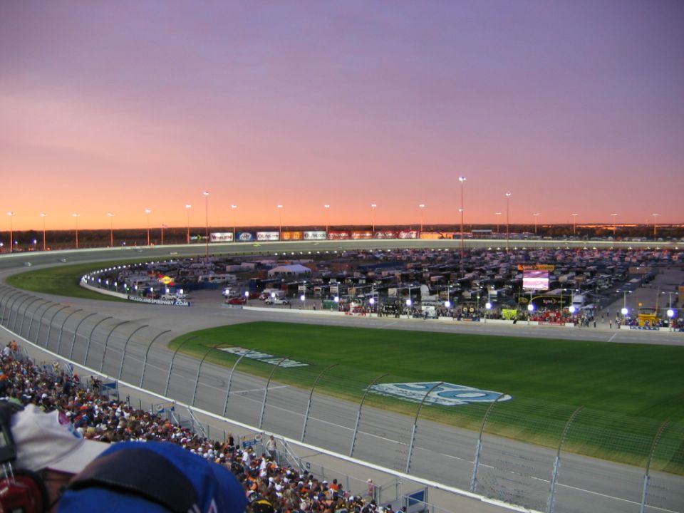 Speedway oval at sunset with crowded grandstands and infield