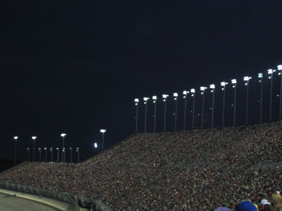 Packed stadium seating under bright lights at a night race