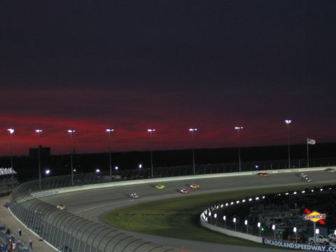 1985 Ford LTD Crown Victoria - Cars race on the Chicagoland Speedway track under a dramatic twilight sky.