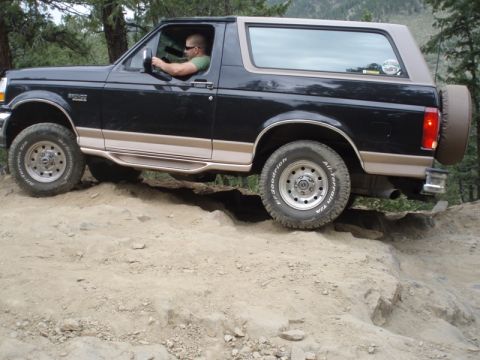 1996 Ford Bronco - A black 1996 Ford Bronco with tan trim navigates a challenging rocky off-road path.