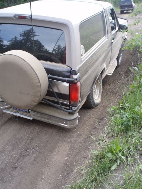 1996 Ford Bronco - A two-tone Ford Bronco navigates a dirt path, with another vehicle following in the distance.