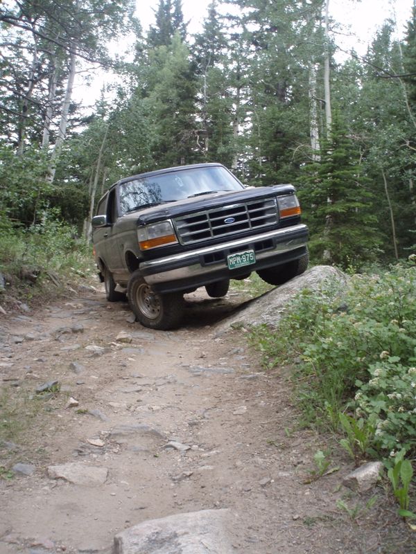 1996 Ford Bronco climbing over a rock on a dirt trail in a forest