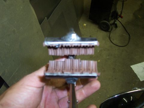 1994 Ford F-150 - A close-up view of a chrome and brown brush part, held by a hand against a backdrop of metal sheeting and equipment.