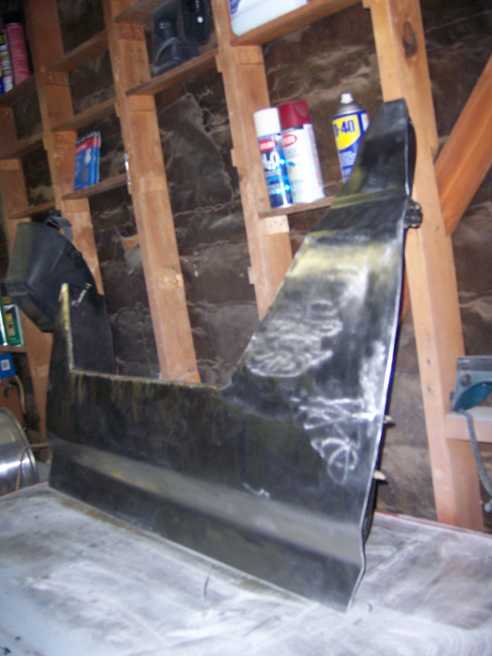 Dark colored car door panel with yellowing on the edge, resting on a surface in a garage