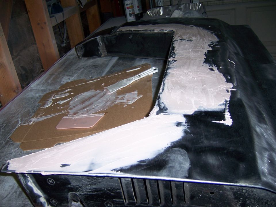 car hood being worked on with body filler and a spreader
