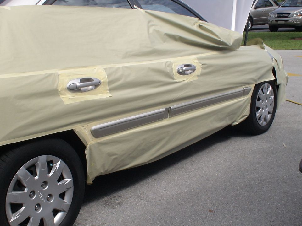car side covered in masking paper, door handles exposed, another car visible in background