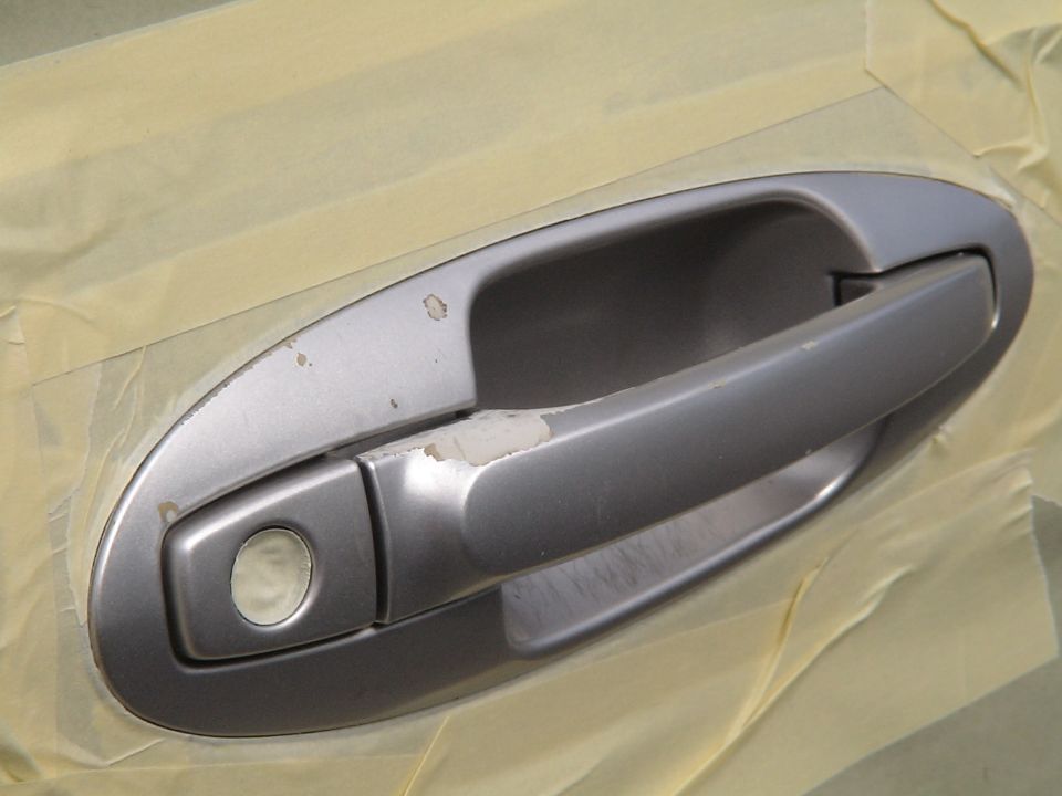 Silver car door handle with paint chips and masking tape