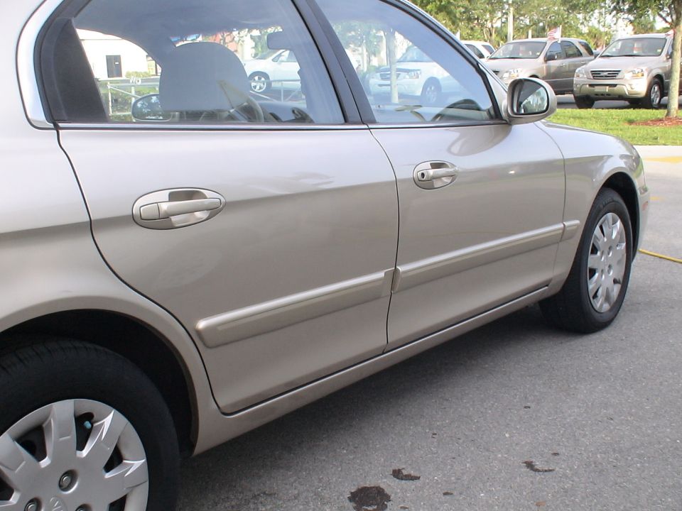 Side view of a tan sedan parked in a lot with other vehicles visible