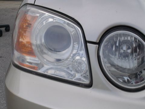 1993 Ford C-350 (Centurion Conversions) - The front corner of a car is visible, focusing on the complex design of the headlight assembly.