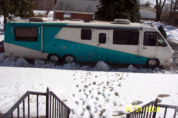 White and teal Class A motorhome parked in snowy yard, side view