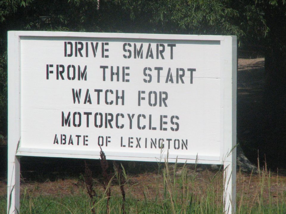 White sign with black text reading "DRIVE SMART FROM THE START WATCH FOR MOTORCYCLES ABATE OF LEXINGTON"