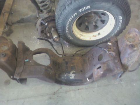 1992 Ford F-350 - A close-up of a heavily rusted vehicle frame part and a tire resting on a concrete surface.
