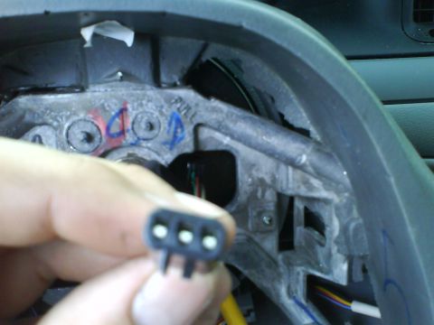 2003 Ford Crown Victoria - A hand holds a three-pin wiring harness connector near the steering column of a 2003 Ford Crown Victoria.