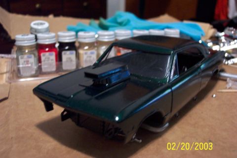 1991 Ford Crown Victoria LTD - A dark green model car with a prominent hood scoop sits on a table next to jars of paint.