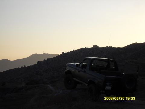 1990 Ford Bronco - A 1990 Ford Bronco is parked on a rocky incline during sunset with mountains in the background.