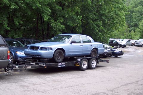 2001 Ford Crown Victoria - A light blue 2001 Ford Crown Victoria is seen on a trailer, with its front bumper removed, parked outdoors.