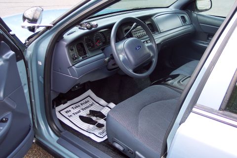 2001 Ford Crown Victoria - Interior view of a 2001 Ford Crown Victoria, likely a police unit, with a 'We Take Pride In Your Vehicle!' floor mat.