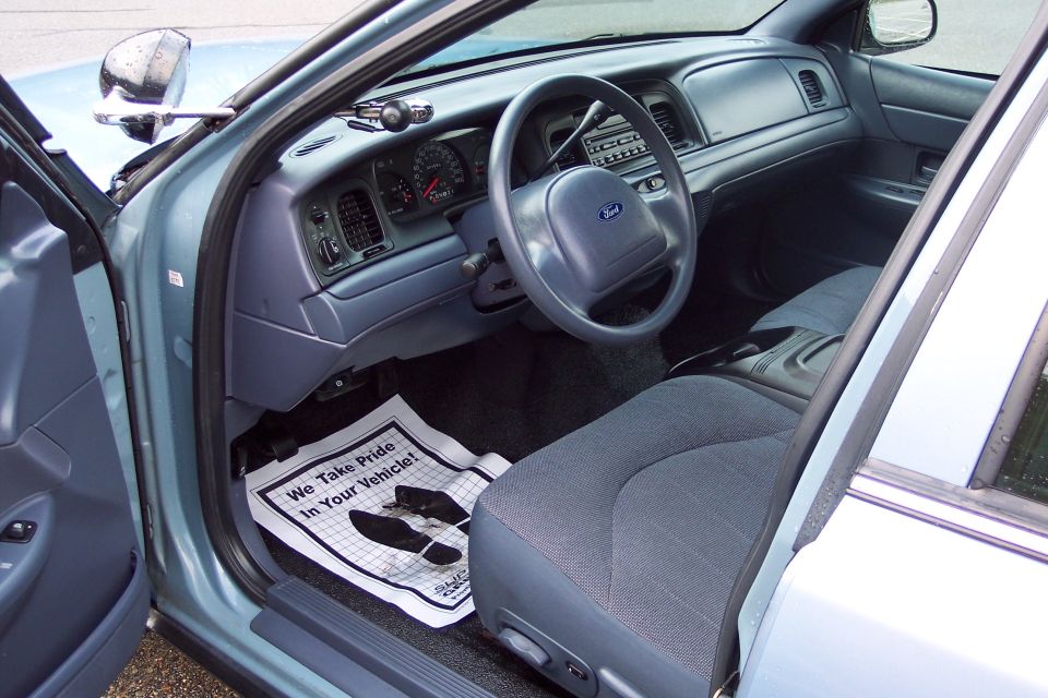 2001 Ford Crown Victoria interior showing dashboard, steering wheel, and front seat. Floor mat reads 'We Take Pride In Your Vehicle!'