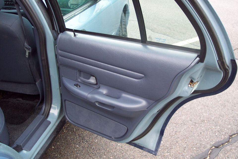 Interior of a light blue Ford Crown Victoria, rear passenger door open, showing dark blue door panel.